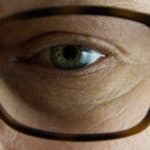 Close-up of a man wearing glasses, showing signs of dry eye discomfort, with redness and irritation visible.