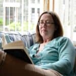 Woman wearing reading glasses while reading a book, representing an ideal candidate for presbyopia eye drop treatment